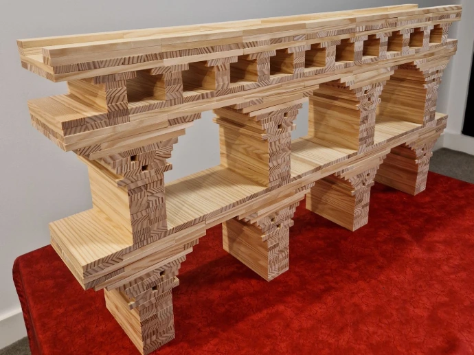 A side-profile view of a double-decker Kapla aqueduct with wide arches on the bottom and smaller, more frequent arches on the top level. The blocks are precisely layered to create smooth curves without any glue or fasteners.